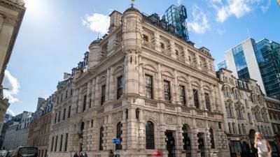 Historic ornate stone building with dome and weathervane in London, modern glass buildings nearby.